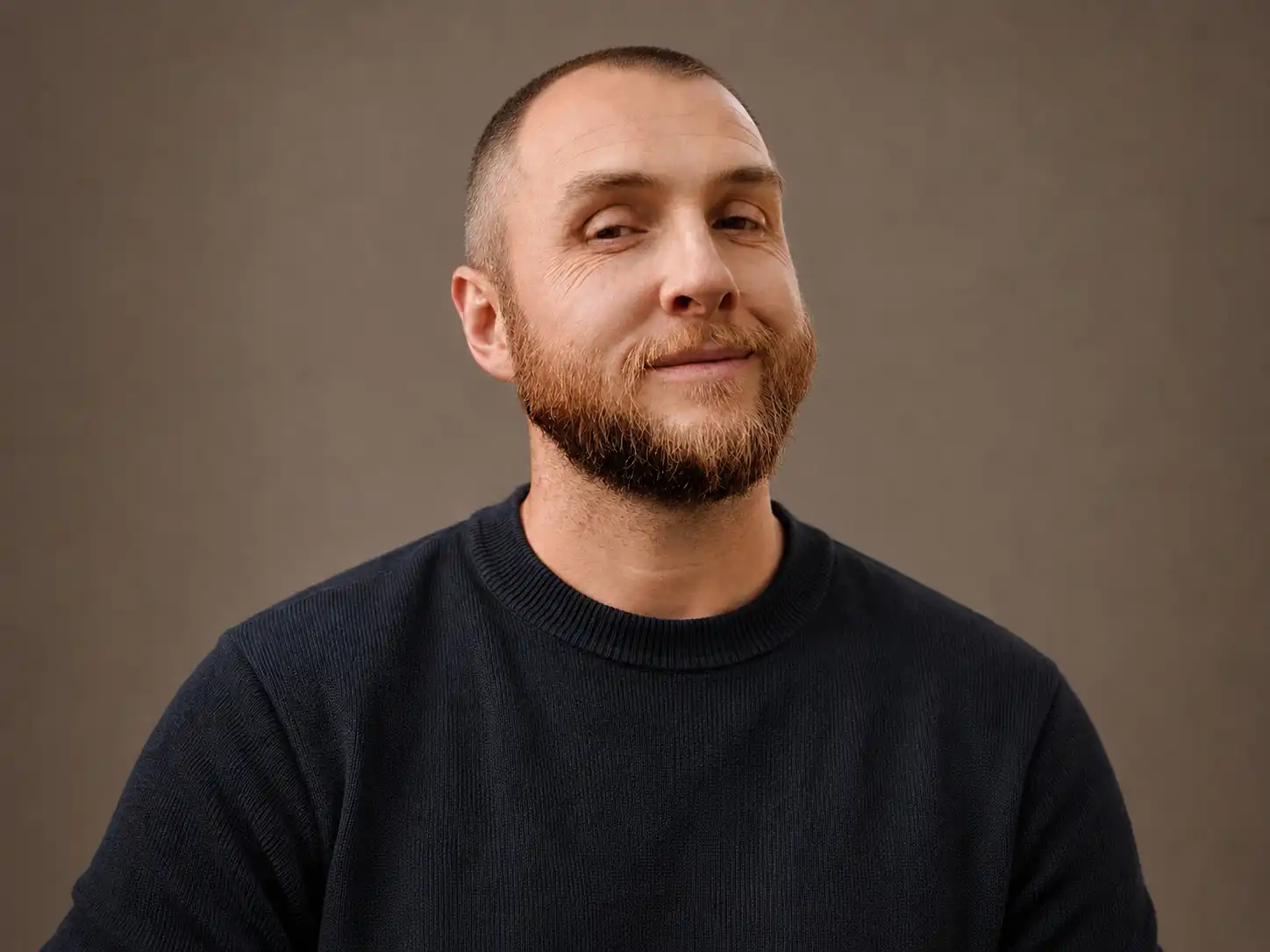 Portrait of Steven Arnold wearing a dark crewneck against a warm neutral background.
